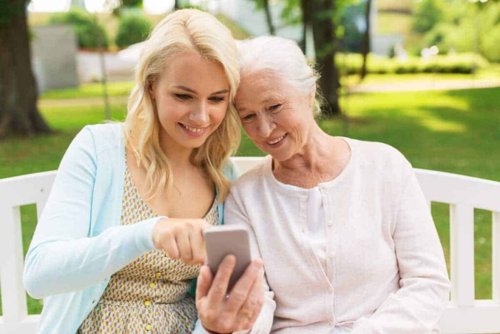 Senior woman sitting outdoors on a bench with her daughter looking at information for Traditions of Hilliard on a smartphone