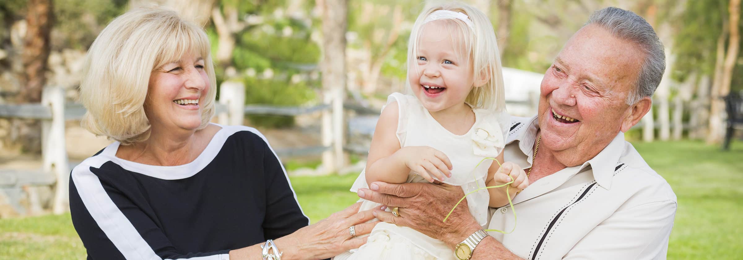 A senior man and senior woman smiling as the man holds his grand daughter while they laugh