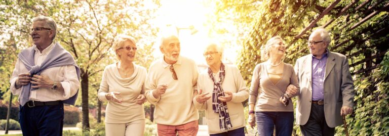 A group of senior men and women walking with their arms linked on a walking path in a park