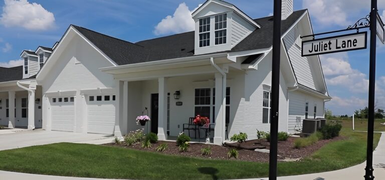 Front view of an independent living garden home for seniors that has a meticulously landscaped lawn and a white brick exterior with a black shingle roof