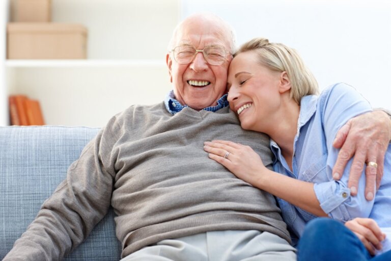 A senior man sitting on the couch with his daughter with his arm around her shoulder