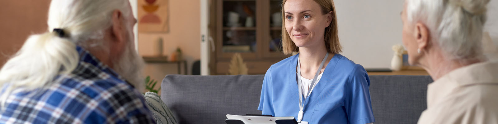 A senior man and woman sitting on a couch speaking to a senior living facility employee during a tour