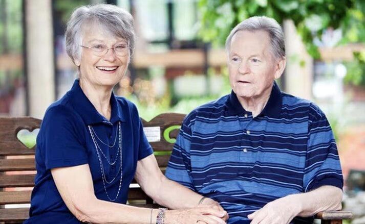Husband and wife sitting together on a bench outdoors at Traditions of Hilliard in Hilliard, Ohio.