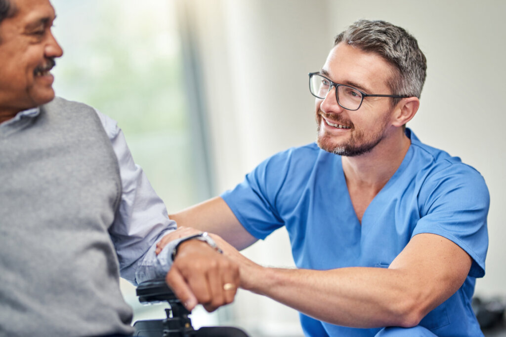 Male nurse smiling and patting the arm of a memory care resident at Traditions of Hilliard in Hilliard, OH.